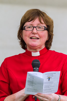 The Reverend Canon Sandie Barton, wearing scarlet, and speaking to a congregation on the green at Barton Mills.